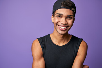 Portrait of smiling latino transgender man in black t-shirt and cap on purple background