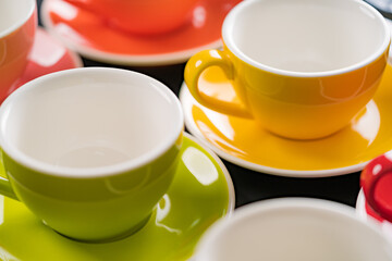 Side view cup of coffee colorful alternating colors is bright Red, Yellow, Orange, Green, Gray, Black and saucer for background in coffee shop.