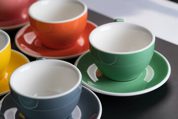 Side view cup of coffee colorful alternating colors is bright Red, Yellow, Orange, Green, Gray, Black and saucer for background in coffee shop.