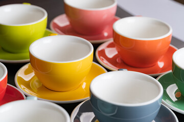 Side view cup of coffee colorful alternating colors is bright Red, Yellow, Orange, Green, Gray, Black and saucer for background in coffee shop.