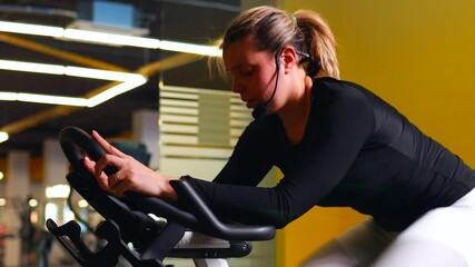 Pretty authentic female instructor with headset in fitness class exercise with group in cycling room