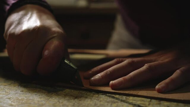 Leather craftsman making at work. Close up of his hands cutting leather using a small knife and a bracket