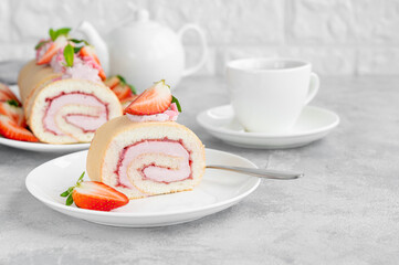 Cake roll with fresh strawberries, jam and cream cheese on a white plate on a gray background. Copy space.