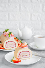 Cake roll with fresh strawberries, jam and cream cheese on a white plate on a gray background. Copy space.