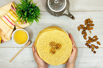 closeup hands holding aMoroccan or Algerian pancakes named Baghrir in arabic plate with honey syrup decorated with walnuts and almond