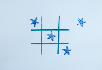 A tic tac toe game with blue sea stars on a pastel blue background. Minimal summer holidays design.