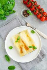 Traditional Italian cannelloni with ricotta and spinach in bechamel sauce with fresh basil leaves on a white plate on a gray concrete background. Vegetarian dish. Copy space.