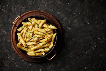 Provencal french fries served in a frying pan on a wooden plate on a dark background