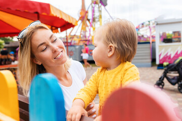 Fototapeta na wymiar Portrait of smiling caucasian young mother with a little daughter. In the background an amusement park. Concept of summer holiday