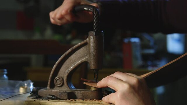 Leather craftsman at work using a hand rivet press in order to puncture leather