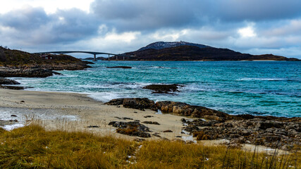 Br&uuml;cke zur Insel Sommaroy in Troms, in der N&auml;he von Troms&ouml;, Norwegen, am Atlantik. gr&uuml;n blaues Meer bei st&uuml;rmischem Wetter, Steine und Sand am Ufer, mit Tang und Gras
