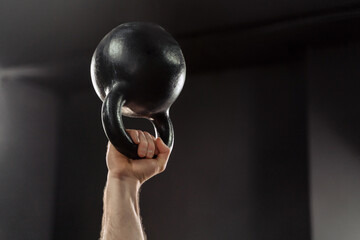 Close up of muscular man's hand holding a kettlebell overhead, doing weightlifting exercises at...