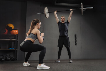Fit caucasian couple doing crossfit exercises at dark gym. Attractive sporty woman doing squats...