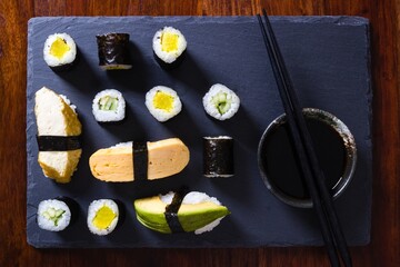 Homemade vegetarian maki and nigiri sushi on slate plate with soy sauce bowl and chopsticks