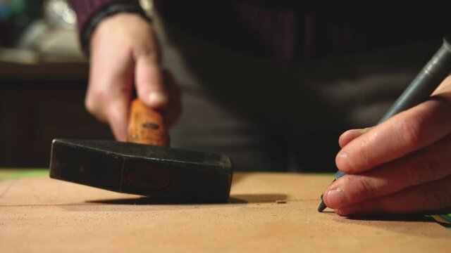 Leather craftsman making at work. Close up of his hands punching leather with a hand rivet and a small hammer