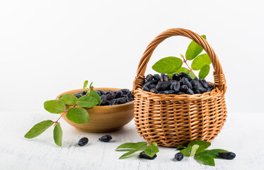 Ripe honeysuckle berries in a basket and in a saucer on a white background
