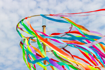 A traditional Maypole with waving colored satin ribbons on blue sky background. Celebrating Summer Solstice and Kupala Night Holiday or Ivan-Kupala. Wooden wheel with ribbons. Selective focus - obrazy, fototapety, plakaty