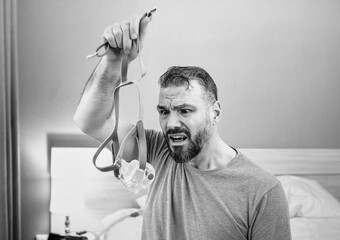 Unhappy shocked man with chronic breathing issues surprised by using  CPAP machine sitting on the bed in bedroom. Healthcare, CPAP, Obstructive sleep apnea therapy, snoring concept