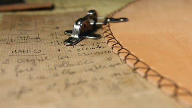 Leather craftsman at work. Rack focus close up of a handwritten project sheet on paper