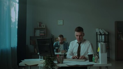 Tired irritated man working in office in evening, angry employee knocking on table and breaking computer with bat, throwing chair, partner taking it on phone. Bad mood, fatigue and failure at work. 