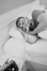 Monochrome portrait of Sleeping man with chronic breathing issues considers using CPAP machine in...