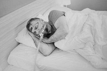 Monochrome portrait of Sleeping man with chronic breathing issues considers using CPAP machine in...