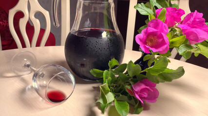 homemade red wine in glass jug, flowers and wine glass on white table in room