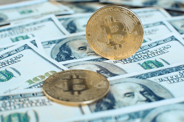 The gold bitcoin cryptocurrency coin stands on its own end, the second one lies on one hundred dollar bills