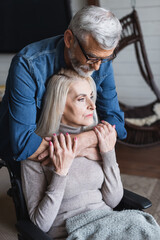 Fototapeta premium Careful man hugging wife in wheelchair at home