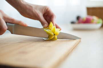 Female hands are holding knife and cutting exotic ripe starfruit or averrhoa carambola. Healthy...