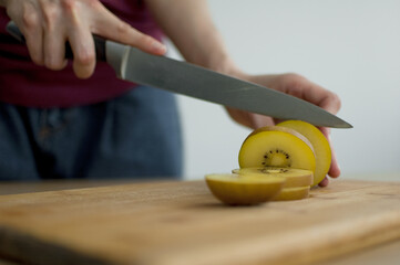 Female hands is cutting a fresh ripe golden kiwi fruit on a cut wooden board. Exotic fruits, healthy eating concept