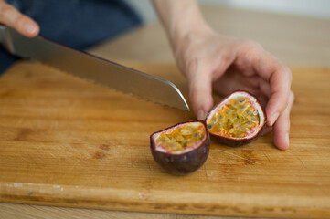 Female hands is cutting a fresh ripe passion fruit, maracuya on a cut wooden board. Exotic fruits, healthy eating concept