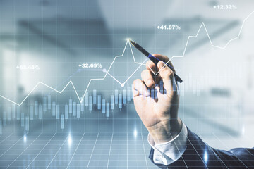 Multi exposure of trader hand with pen working with virtual abstract financial graph interface on blurred office background, financial and trading concept