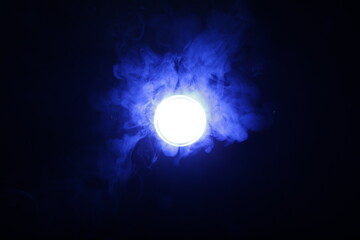 Artificial magic blue light illuminates smoke on dark background