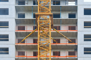 Construction site with middle part of  tall crane tower attached to facade of house under...