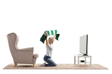 Casual young female at home watching a match and cheering with a scarf in front of tv