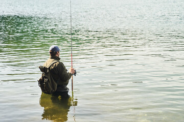 Fisher man stands in the water and catch fish in the lake on a background of mountains