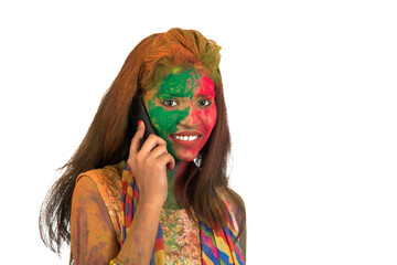 Young girl with colorful face talking on phone and celebrating festival of color Holi.