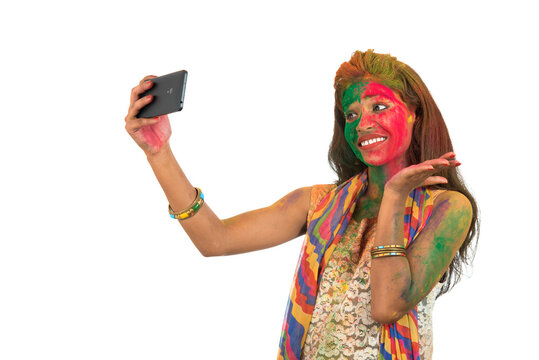 Young girl with colourful face taking selfie using smartphone on Holi festival. Festival and technology concept on white background.