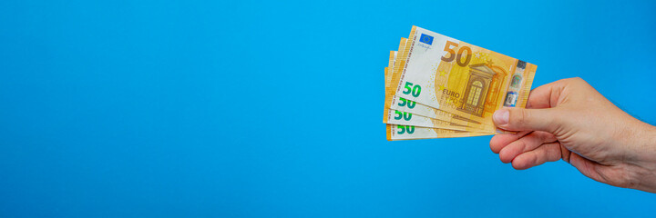 Money in hand, poster with banknote in hand. Hand holding 50 euro banknotes isolated on blue background. Banner with blue background on financial themes
