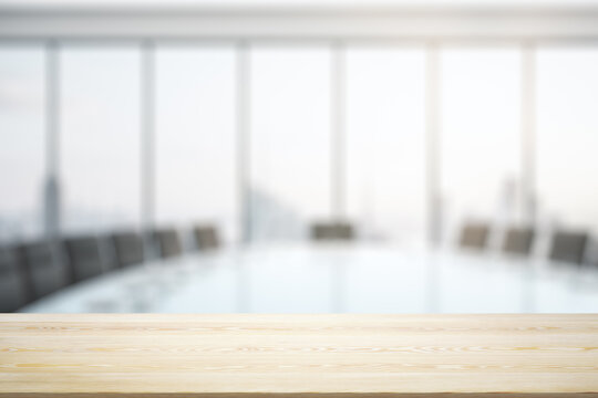 Blank wooden office desk with light furnished meeting room with big window on background, mock up