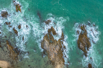 Aerial top view of white waves in green sea hit on the large rocks in summer day. .Beach sea space area. green sea, waves crashing on the rocks.. At Kalim Beach Phuket Thailand.