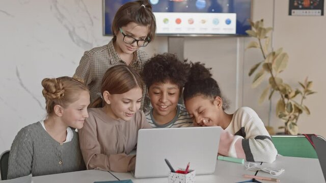Medium slowmo of group of multiethnic 5-grade students having fun while doing task or watch video on laptop in modern Science class of contemporary school