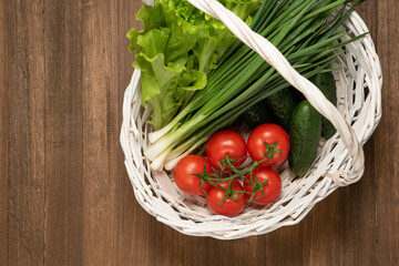 vegetables in a basket on a wooden background. lettuse, scallion, cucumbers and tomatoes