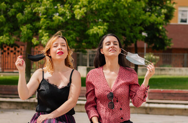 Two women taking off their masks on the street. Concept end of the mandatory outdoor mask. End of the pandemic. Friends.