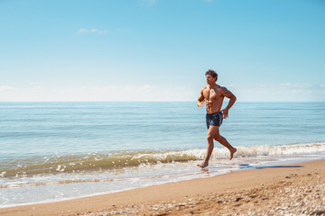 Young muscular guy, with a bare torso running along the beach