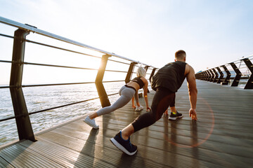 Young fitness couple is doing workout at the beach pier. Young man and woman doing exercises...