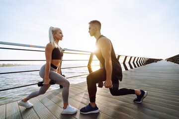 Young fitness couple is doing workout at the beach pier. Young man and woman doing exercises outdoors in the morning. Sport, Active life. 