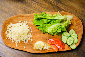 grated cheese, lettuce, ringed tomato and cucumber on a wooden cutting board.