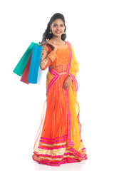 Fototapeta premium Beautiful Indian young girl holding shopping bags while wearing traditional ethnic wear. Isolated on a white background
